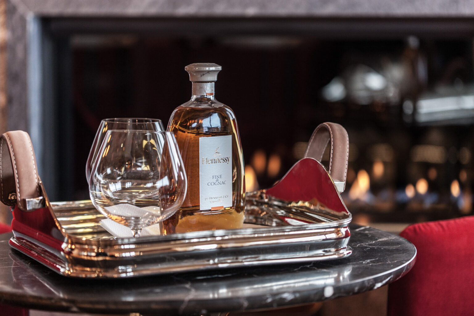 A polished silver tray holds a whiskey bottle and a glass in a cozy setting, with a warm fireplace in the background, creating an inviting atmosphere for relaxation and enjoyment. | Only on SopranoVillas