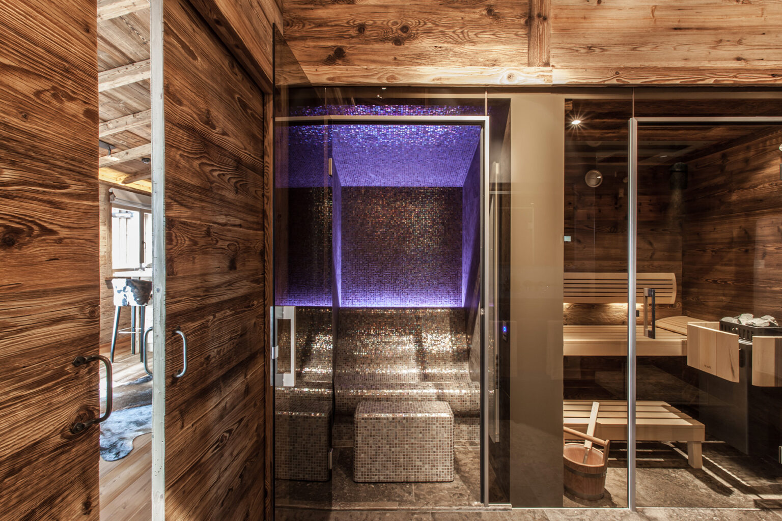 Modern sauna interior featuring a sleek glass enclosure, illuminated by purple LED lighting, set against rustic wooden walls and flooring, designed for relaxation and wellness. | Only on SopranoVillas