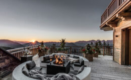 Mountain view deck with a cozy fire pit, surrounded by comfortable seating and potted plants, showcasing a stunning sunset over the peaks.
