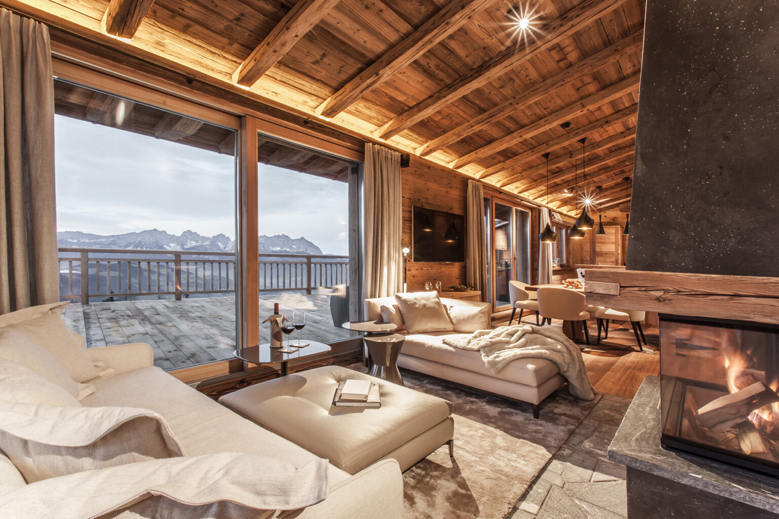 Luxurious mountain chalet interior featuring a cozy living area with a fireplace, large windows showcasing scenic views, wooden beams, and elegant furnishings. Perfect for a relaxing getaway in nature. | Only on SopranoVillas