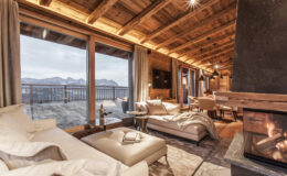 Luxurious mountain chalet interior featuring a cozy living area with a fireplace, large windows showcasing scenic views, wooden beams, and elegant furnishings. Perfect for a relaxing getaway in nature.