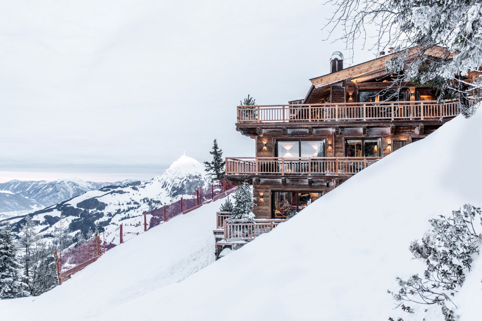 Charming wooden chalet nestled on a snow-covered slope, surrounded by majestic mountains, offering a picturesque winter getaway. | Only on SopranoVillas