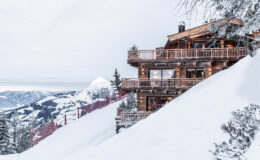 Charming wooden chalet nestled on a snow-covered slope, surrounded by majestic mountains, offering a picturesque winter getaway.