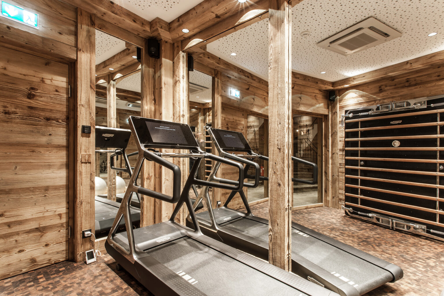Modern home gym featuring two treadmills and wooden decor, designed for fitness enthusiasts. Mirrors enhance the spacious feel, creating an inviting workout environment. | Only on SopranoVillas