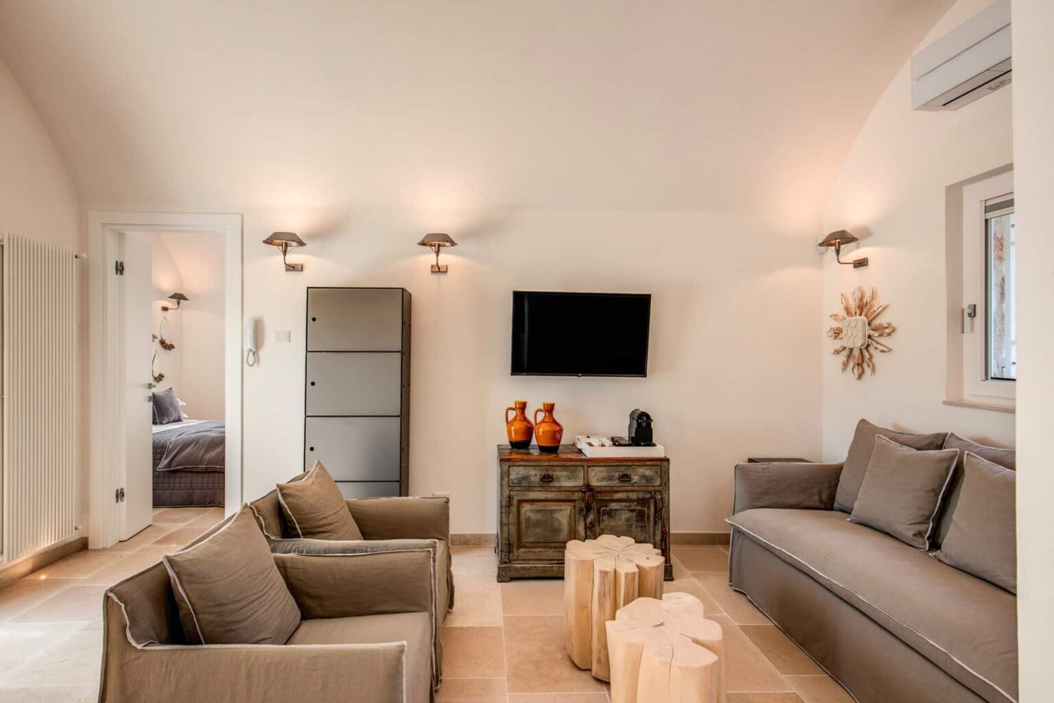Modern living room featuring a comfortable gray sofa and armchairs, a wooden coffee table, a flat-screen TV mounted on the wall, and warm lighting, creating a cozy atmosphere. | Only on SopranoVillas