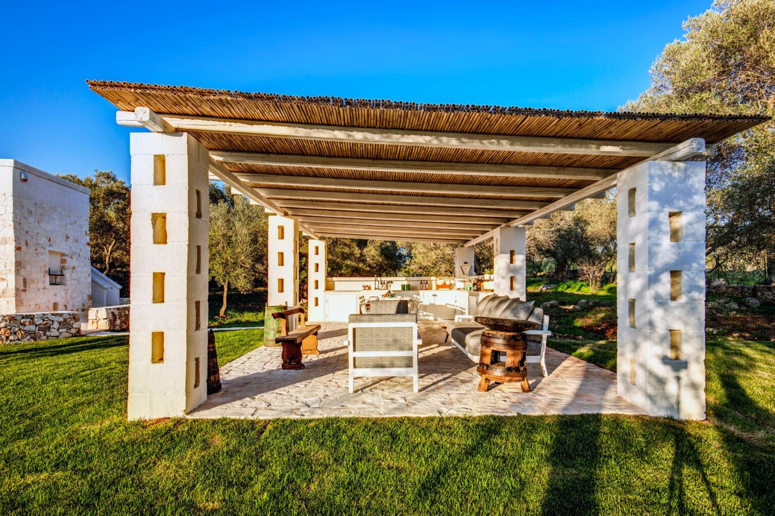 Outdoor seating area with a rustic design, featuring a thatched roof, white furniture, and surrounded by lush greenery, perfect for relaxation and gatherings in a serene environment. | Only on SopranoVillas