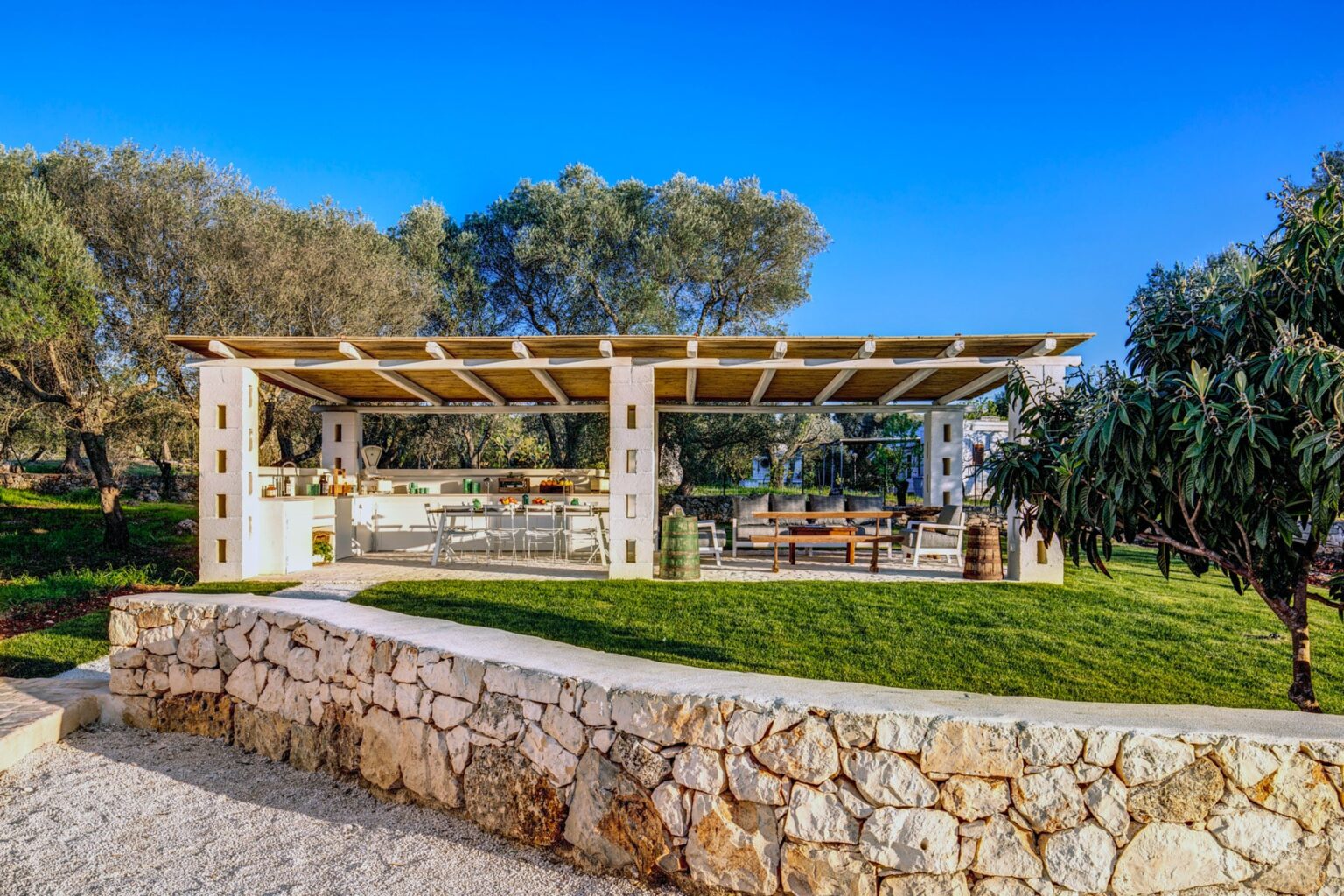Outdoor dining area featuring a modern pergola surrounded by lush greenery and stone walls, ideal for gatherings and events. | Only on SopranoVillas