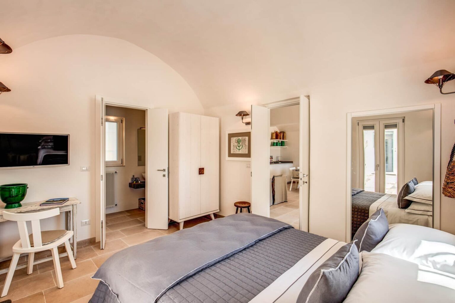 Modern hotel room featuring a cozy design with two beds, a flat-screen TV, and an en-suite bathroom. The space includes natural light from large windows, a small table, and stylish decor elements. | Only on SopranoVillas