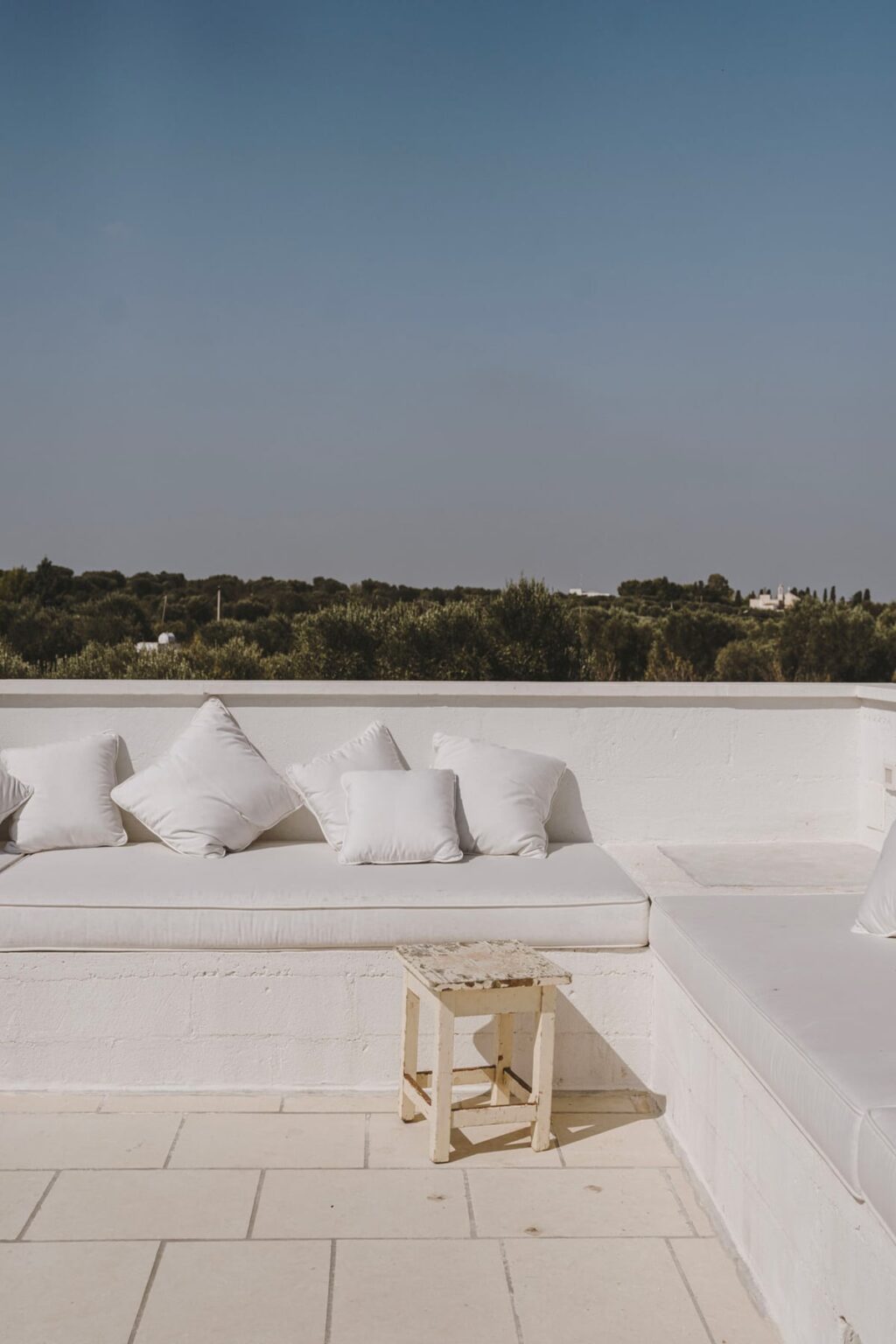 Stylish outdoor seating area featuring a white sofa adorned with plush cushions, overlooking a lush green landscape under a clear sky. Ideal for relaxation and outdoor gatherings. | Only on SopranoVillas