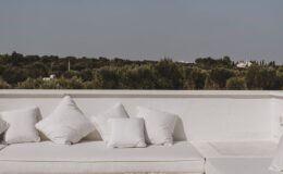 Stylish outdoor seating area featuring a white sofa adorned with plush cushions, overlooking a lush green landscape under a clear sky. Ideal for relaxation and outdoor gatherings.
