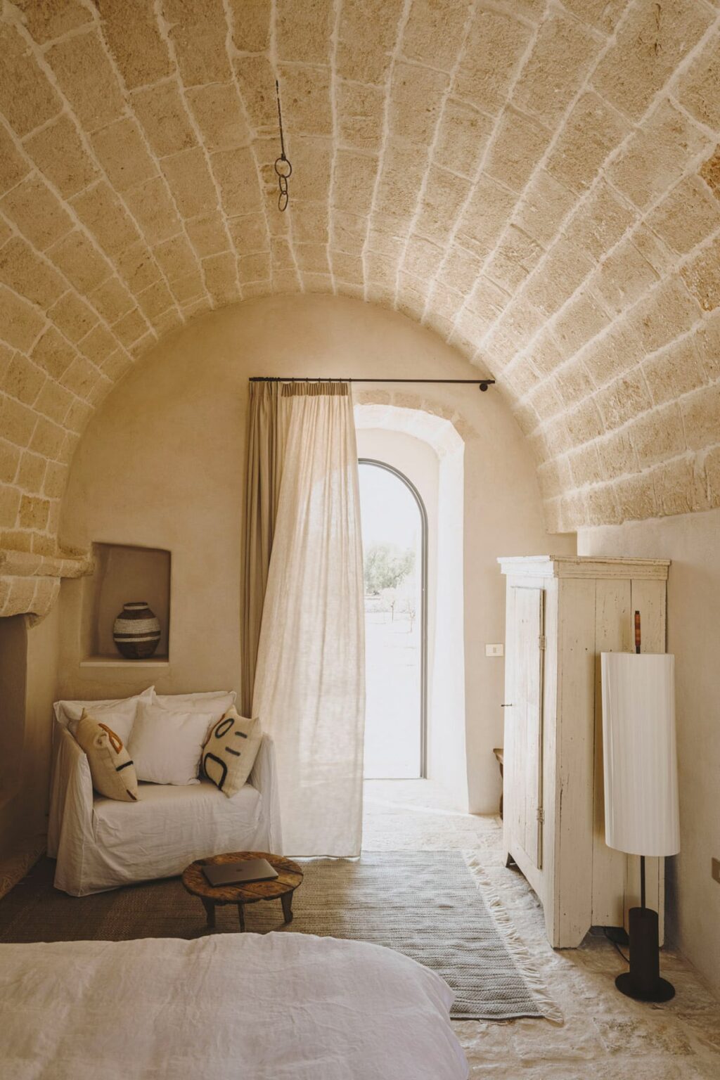 Cozy interior of a rustic room featuring an arched stone ceiling, soft beige walls, a large window with sheer curtains, and minimalist decor, creating a warm and inviting atmosphere. | Only on SopranoVillas