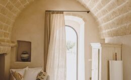 Cozy interior of a rustic room featuring an arched stone ceiling, soft beige walls, a large window with sheer curtains, and minimalist decor, creating a warm and inviting atmosphere.