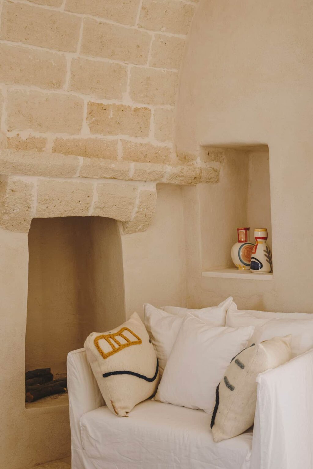Cozy interior of a rustic room featuring a stone fireplace, soft bedding, and decorative pottery displayed in a niche, highlighting a warm and inviting atmosphere. | Only on SopranoVillas