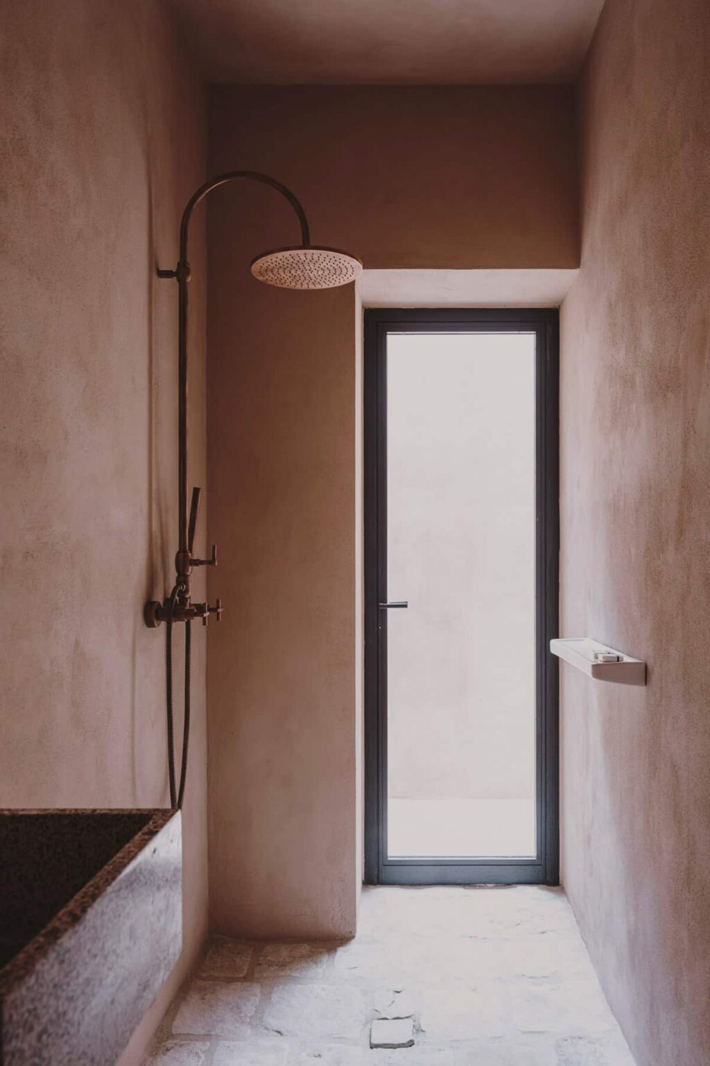 Modern bathroom interior featuring a minimalist design with a shower on the left and a sleek door leading outside. The walls are finished in a soft, neutral tone, creating a serene atmosphere. | Only on SopranoVillas
