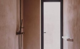 Modern bathroom interior featuring a minimalist design with a shower on the left and a sleek door leading outside. The walls are finished in a soft, neutral tone, creating a serene atmosphere.