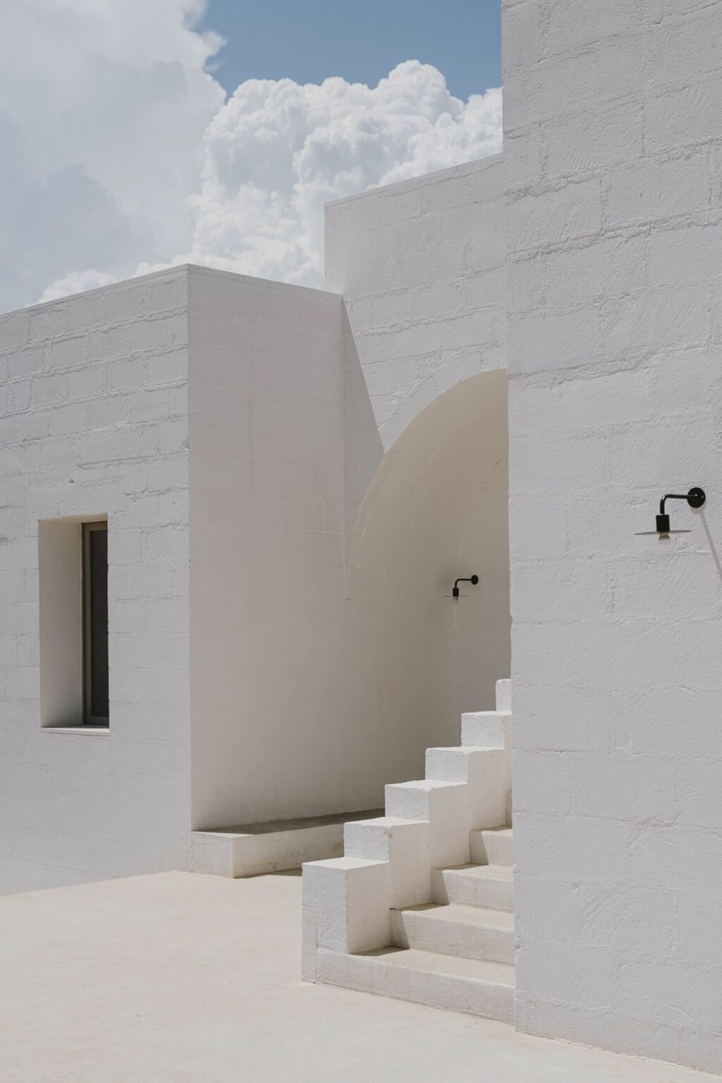 Modern white architecture featuring a textured wall, arched entrance, and minimalist design elements, illuminated by stylish outdoor sconces. | Only on SopranoVillas
