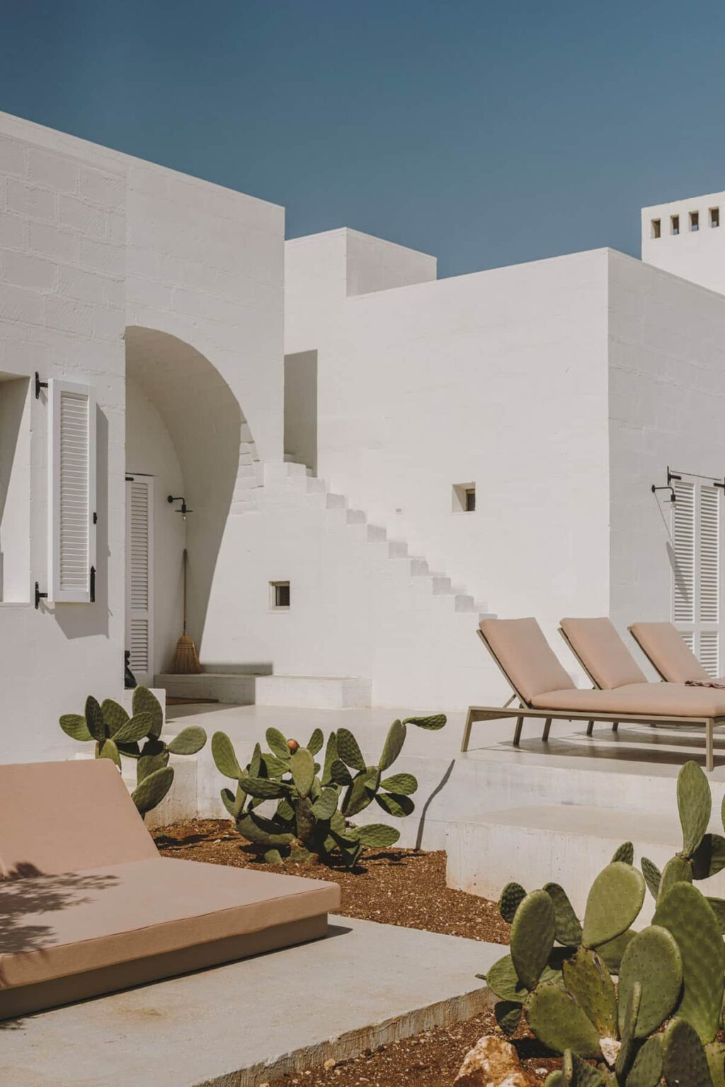 Modern white architectural design featuring a staircase, lounging chairs, and minimalistic decor, set in a serene outdoor environment. | Only on SopranoVillas