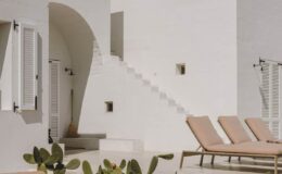 Modern white architectural design featuring a staircase, lounging chairs, and minimalistic decor, set in a serene outdoor environment.