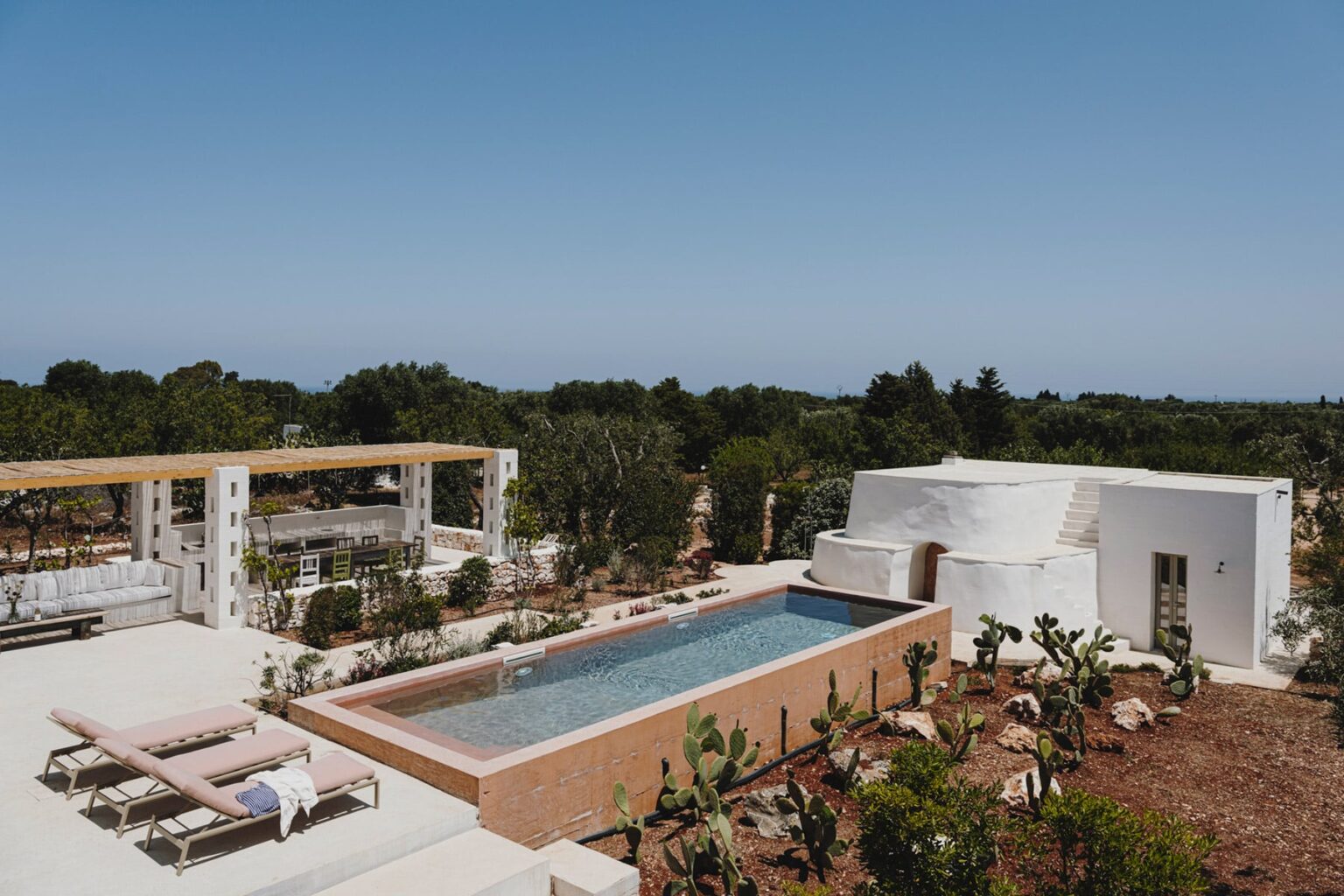 Modern villa with a swimming pool surrounded by lush greenery, featuring outdoor seating and a pergola, ideal for relaxation and outdoor living. | Only on SopranoVillas