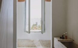 Bright bathroom with open window offering a scenic view, featuring a stone sink and modern light fixtures.