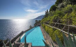 Stunning infinity pool overlooking the serene ocean, surrounded by lush greenery and rocky cliffs, under a bright blue sky. Perfect for luxury vacation relaxation.