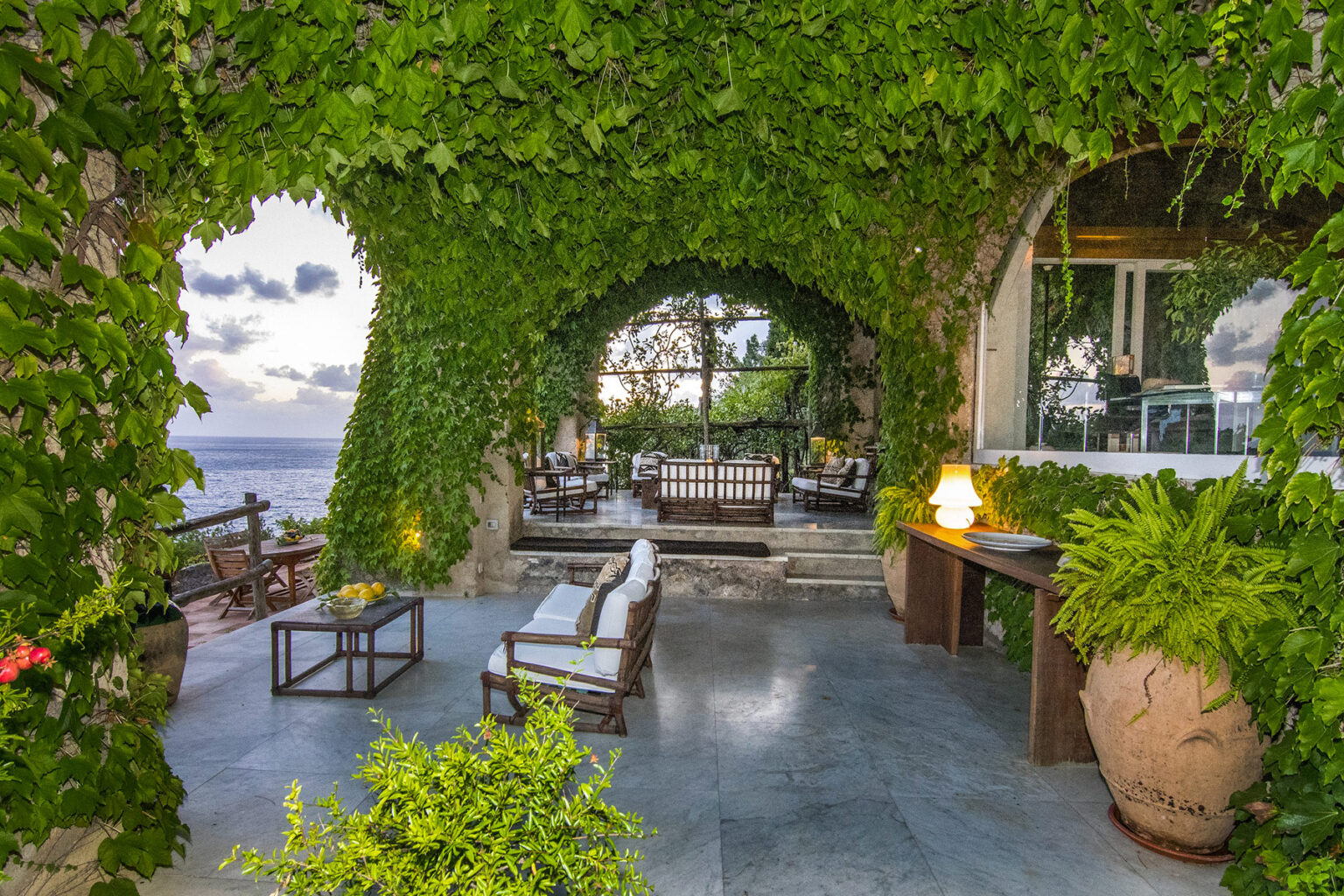 Luxurious outdoor patio surrounded by lush greenery, featuring comfortable seating and a stunning ocean view. Ideal for relaxation and entertaining in a serene environment. | Only on SopranoVillas