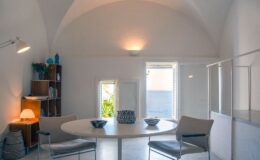 Bright and airy dining area with a round table, modern chairs, and a minimalist design, featuring large windows that let in natural light and a view of greenery.