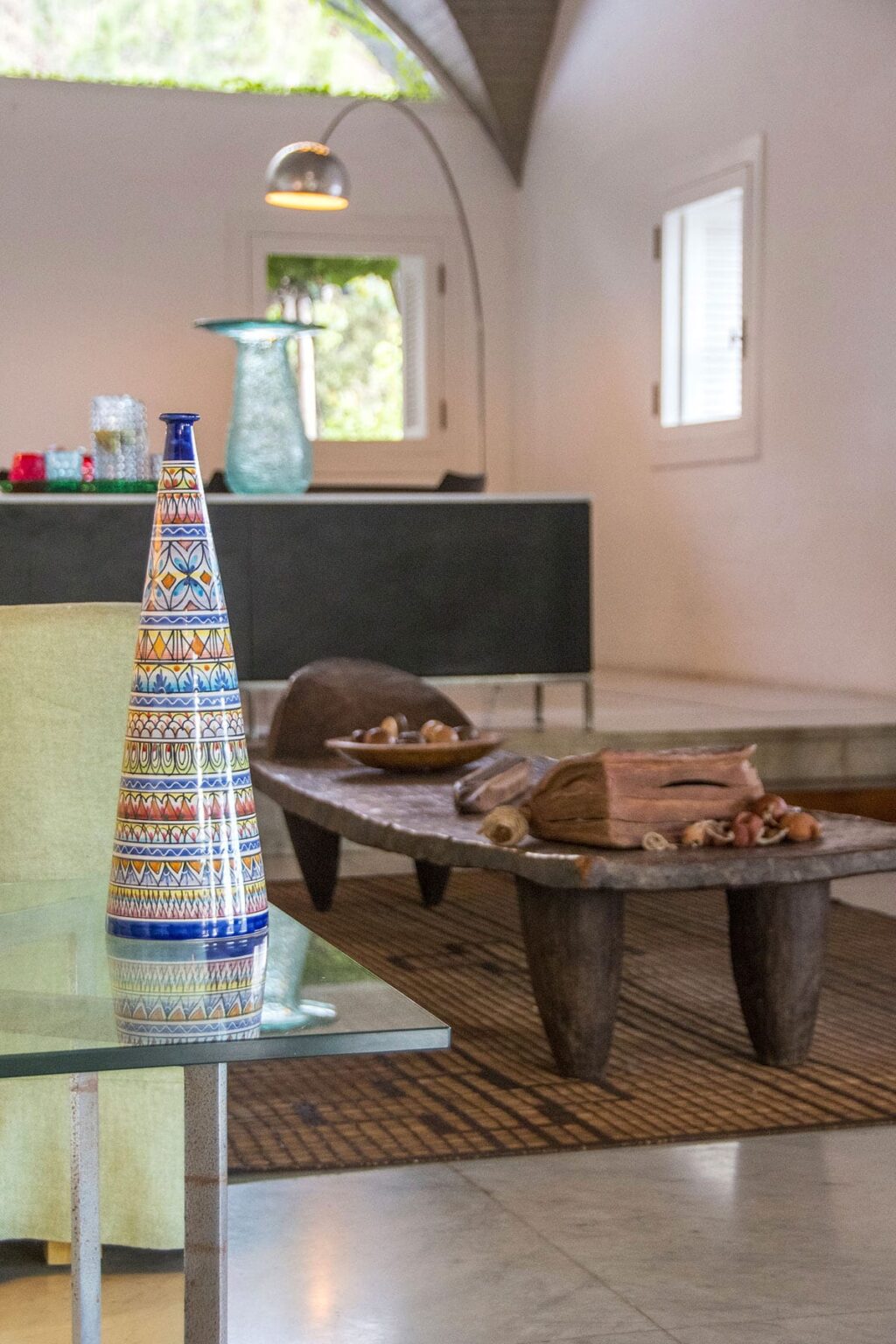 Colorful ceramic vase with intricate patterns next to a rustic wooden coffee table adorned with decorative stones and wood pieces, set in a modern interior space. | Only on SopranoVillas