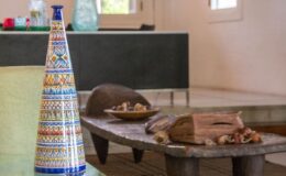 Colorful ceramic vase with intricate patterns next to a rustic wooden coffee table adorned with decorative stones and wood pieces, set in a modern interior space.
