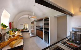 Spacious modern kitchen featuring arched ceilings, wooden cabinetry, stainless steel appliances, and a variety of fresh ingredients on the counter, creating an inviting culinary atmosphere.