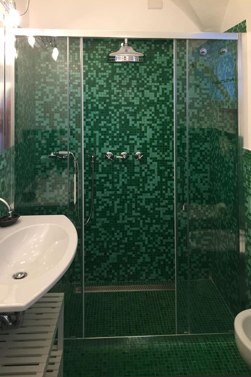 Modern bathroom design featuring a green mosaic tile shower with glass doors, complemented by a sleek white sink. | Only on SopranoVillas