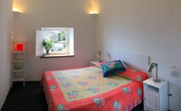 Cozy bedroom featuring a colorful floral bedspread, bedside tables with lamps, and a window with natural light illuminating the space. Ideal for relaxation and comfort.
