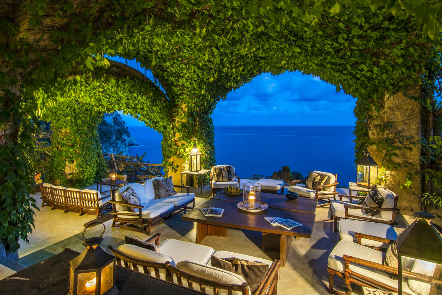 Cozy outdoor living area with comfortable seating and a stunning ocean view, framed by lush greenery and evening sky. Perfect for relaxation and entertaining. | Only on SopranoVillas
