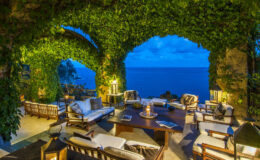 Cozy outdoor living area with comfortable seating and a stunning ocean view, framed by lush greenery and evening sky. Perfect for relaxation and entertaining.