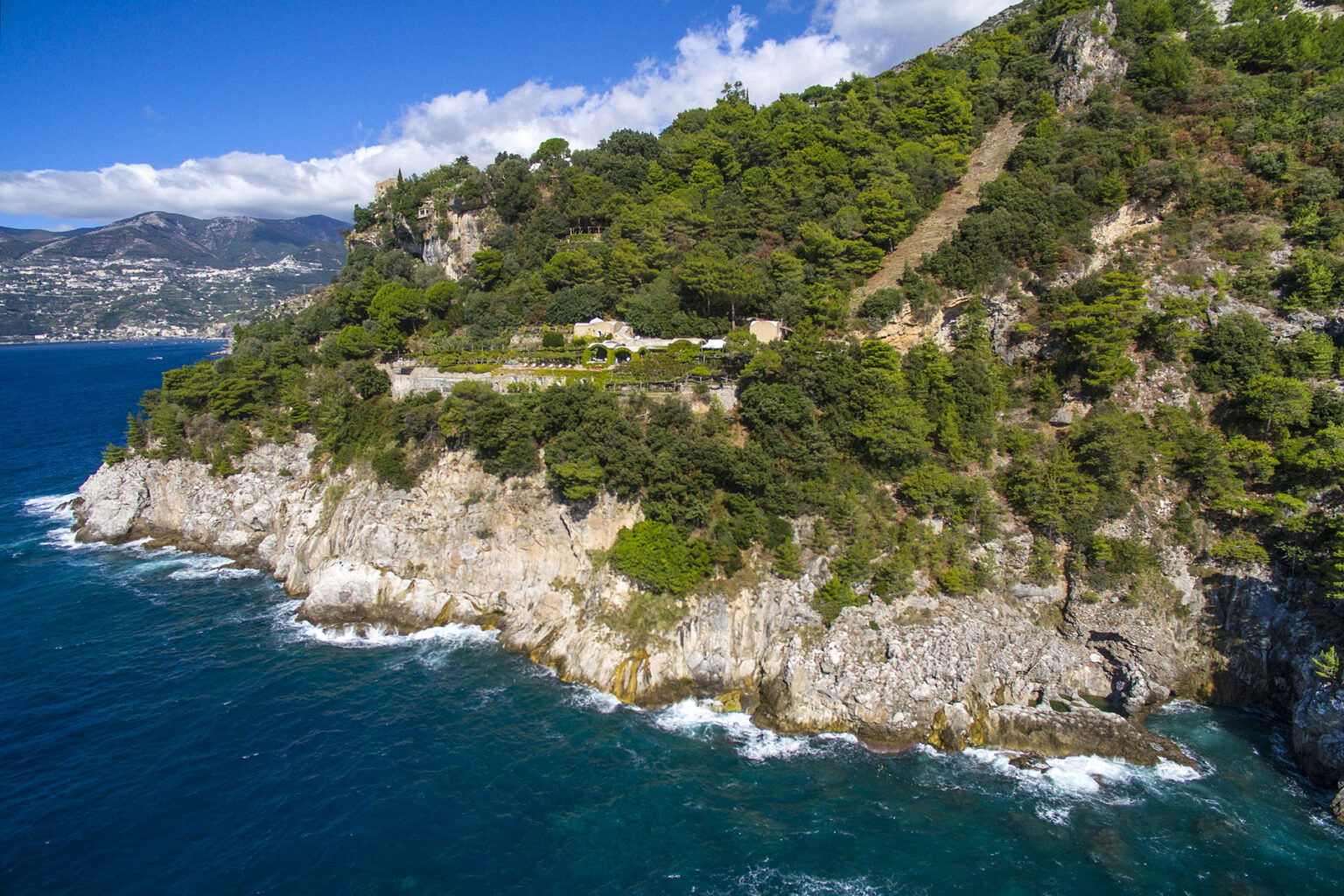 Aerial view of a rocky coastline with lush green vegetation and a scenic ocean backdrop, showcasing a tranquil coastal landscape. | Only on SopranoVillas