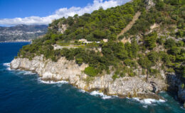 Aerial view of a rocky coastline with lush green vegetation and a scenic ocean backdrop, showcasing a tranquil coastal landscape.