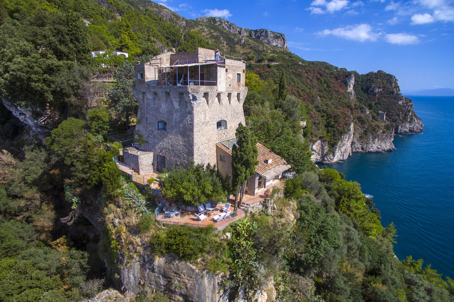 Historic stone tower overlooking the coastline, surrounded by lush greenery and offering a panoramic view of the sea, ideal for vacation rentals or photography. | Only on SopranoVillas