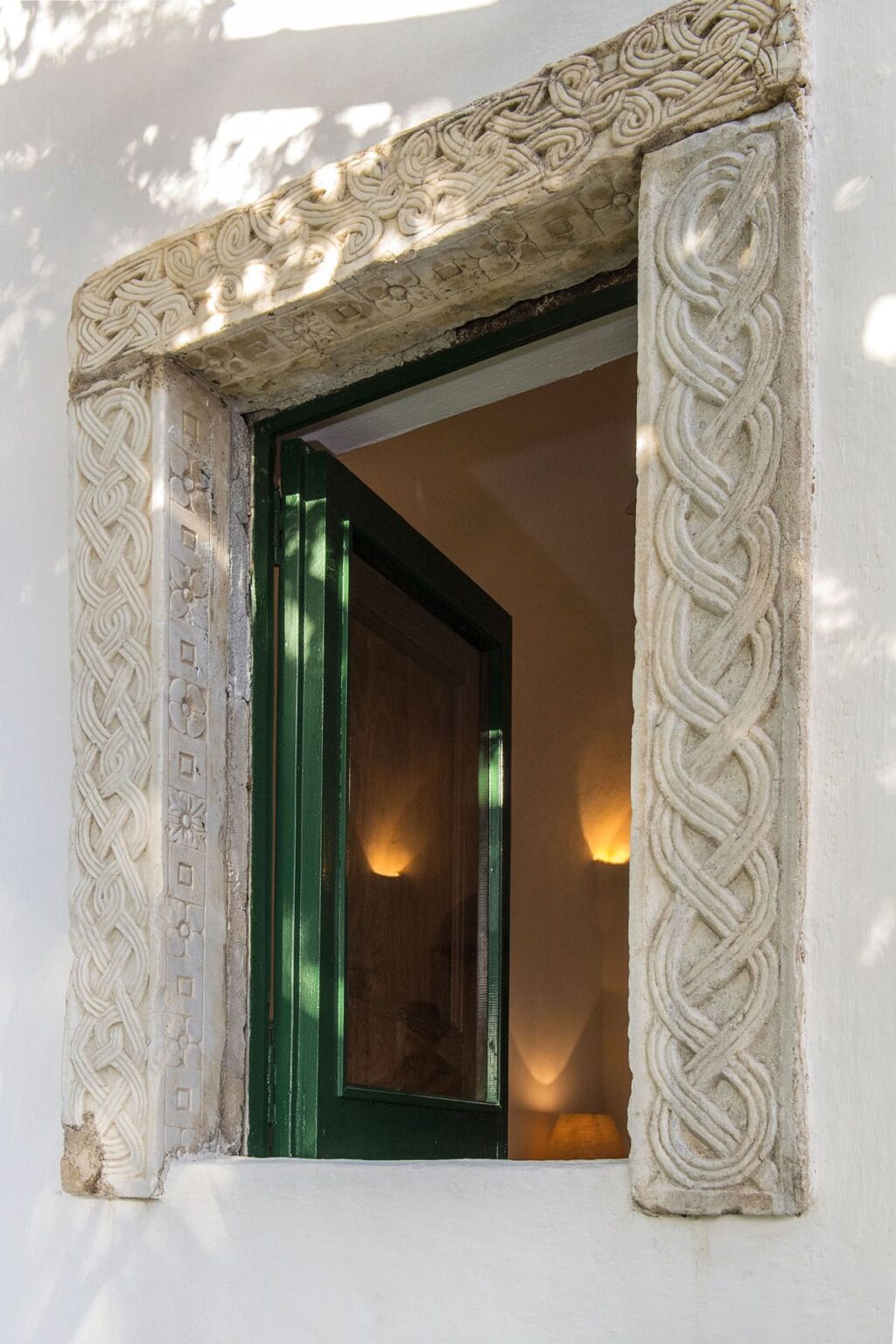 Intricately designed stone door frame featuring a braided pattern, leading to a warmly lit interior space with a green door. | Only on SopranoVillas