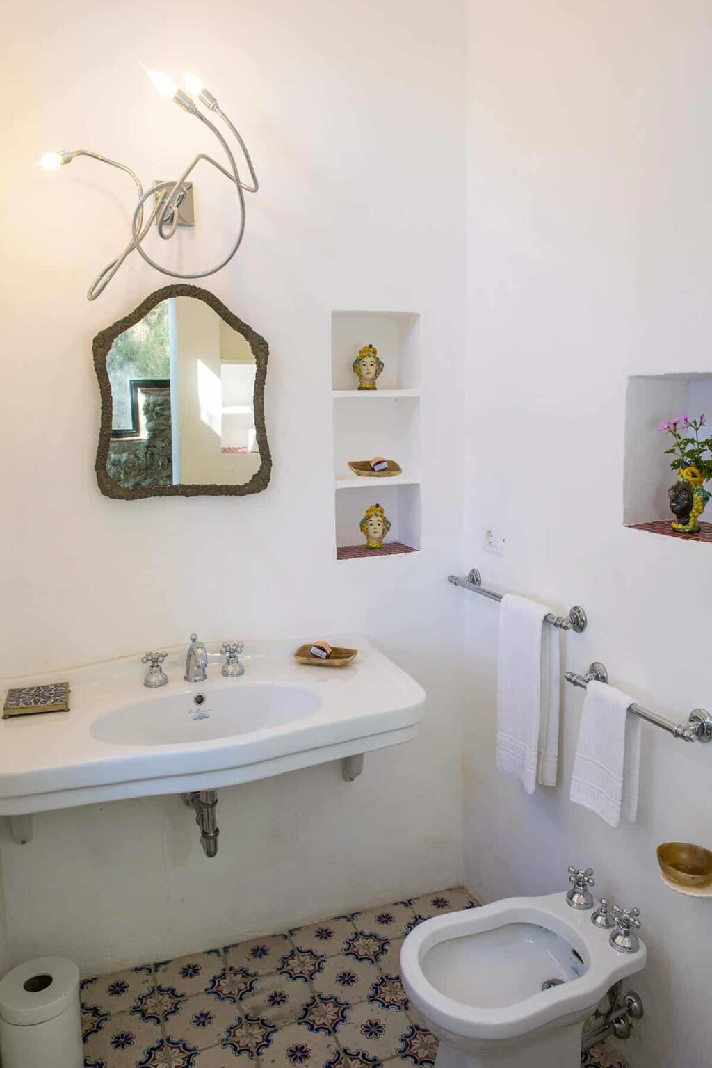Modern bathroom featuring a stylish sink with a vintage mirror, decorative shelves displaying small sculptures, and neatly arranged towels, creating an elegant and inviting atmosphere. | Only on SopranoVillas