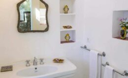 Modern bathroom featuring a stylish sink with a vintage mirror, decorative shelves displaying small sculptures, and neatly arranged towels, creating an elegant and inviting atmosphere.