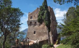 Historic stone tower surrounded by lush greenery and trees, overlooking a scenic landscape with mountains and a body of water. Ideal for travel and architectural history enthusiasts.