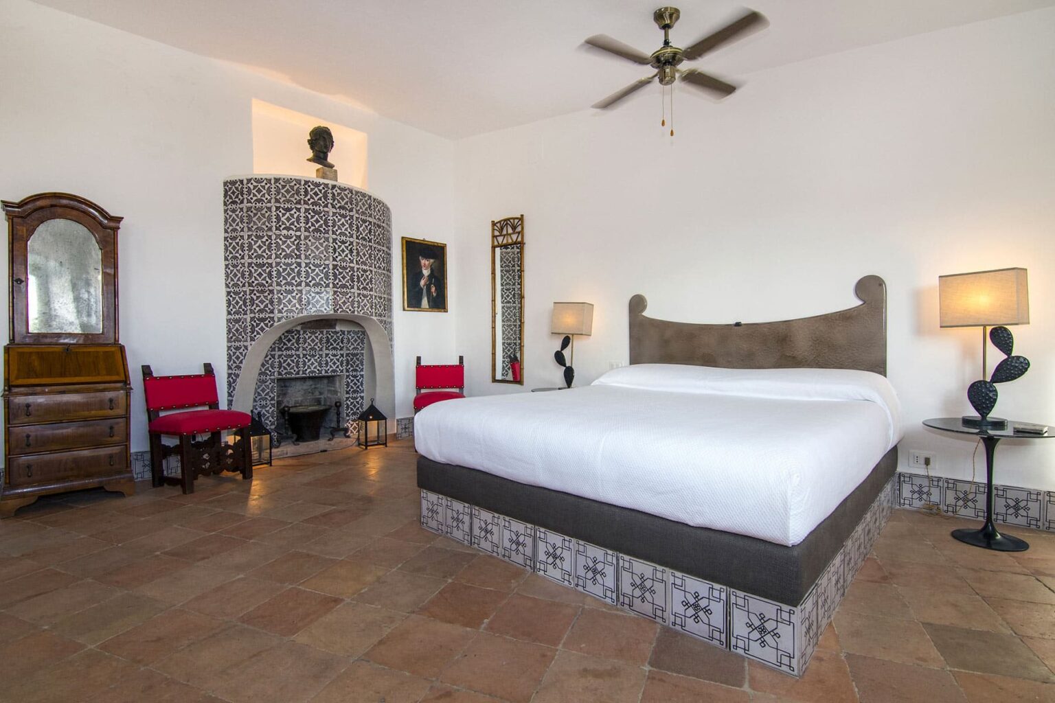 Spacious and stylish bedroom featuring a large bed, decorative tile accents, wooden furniture, and a cozy fireplace, ideal for relaxation and comfort. | Only on SopranoVillas
