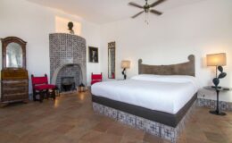 Spacious and stylish bedroom featuring a large bed, decorative tile accents, wooden furniture, and a cozy fireplace, ideal for relaxation and comfort.