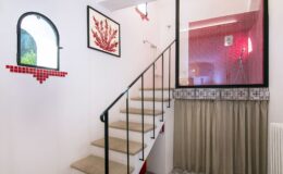 Modern staircase with a decorative wall featuring red accents and artwork, leading to a stylish upper level in a contemporary home. The interior design combines clean lines with vibrant colors, creating an inviting atmosphere.
