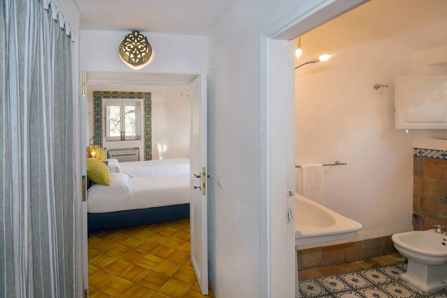 Interior view of a hotel room showcasing a doorway leading to a cozy bedroom with two beds and a well-lit bathroom featuring a bathtub and modern amenities. | Only on SopranoVillas