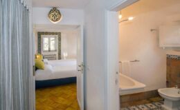 Interior view of a hotel room showcasing a doorway leading to a cozy bedroom with two beds and a well-lit bathroom featuring a bathtub and modern amenities.