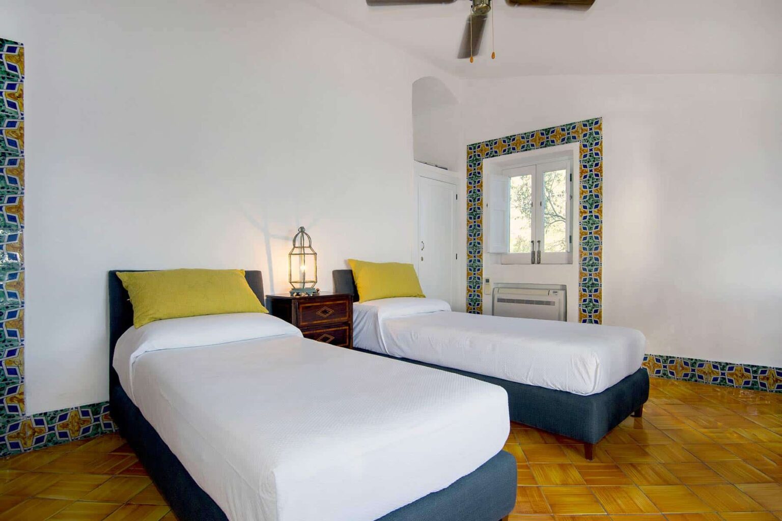 Bright and airy bedroom featuring two twin beds with yellow accent pillows, wooden flooring, and decorative tiled walls, ideal for a comfortable stay. | Only on SopranoVillas
