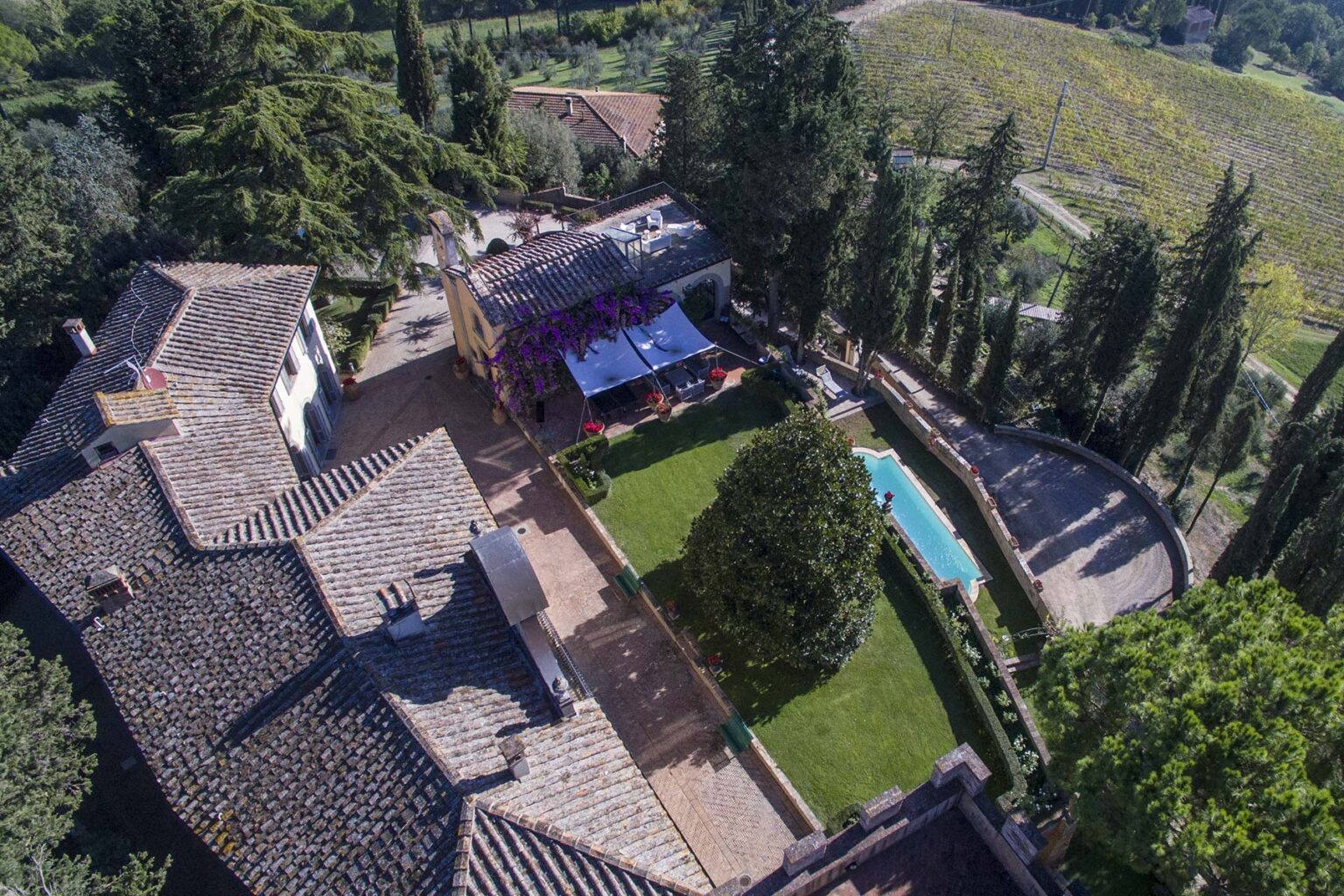 Aerial view of a luxurious villa surrounded by lush greenery, featuring a swimming pool, well-maintained garden, and outdoor seating area, set against a scenic landscape. | Only on SopranoVillas