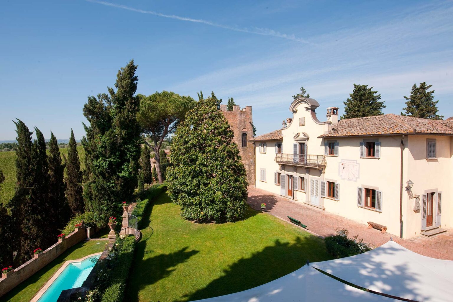 Aerial view of a charming villa surrounded by lush greenery, featuring a swimming pool and a well-maintained garden under a clear blue sky. | Only on SopranoVillas