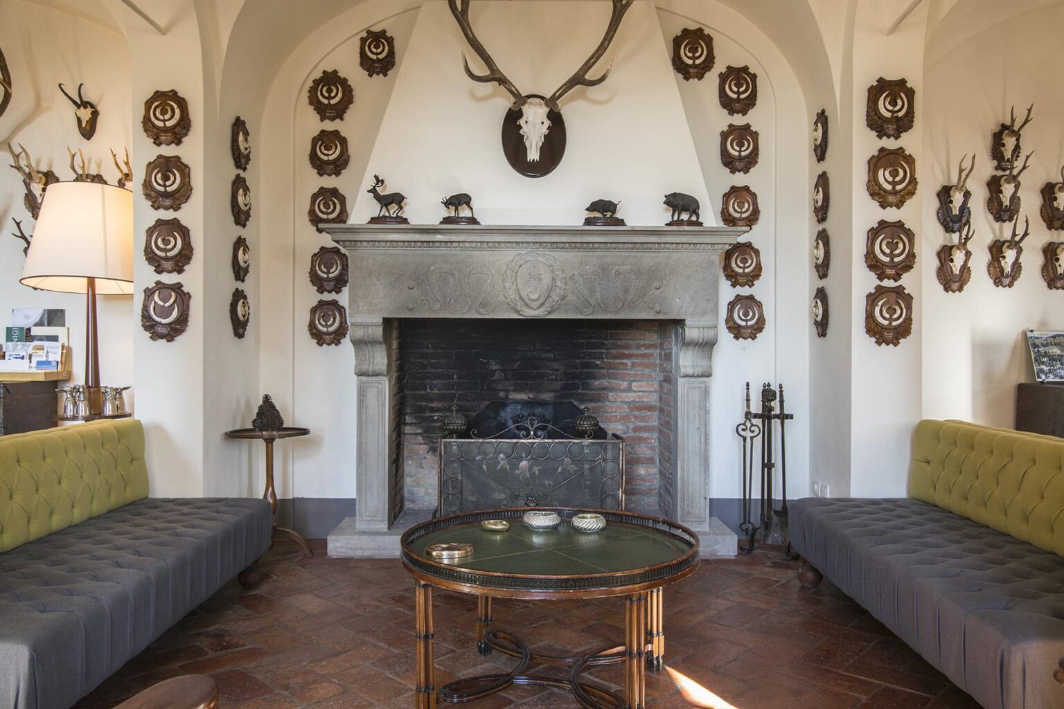 Cozy living room featuring a stone fireplace, two gray sofas, and a round coffee table, adorned with mounted deer antlers and decorative plaques on the walls. | Only on SopranoVillas